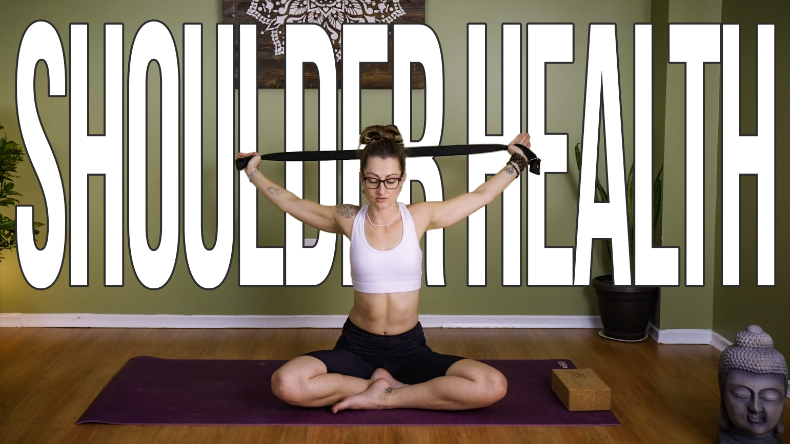 Carole Carter from Living Lotus Online sitting cross legged on a yoga mat demonstrating shoulder floss with yoga strap